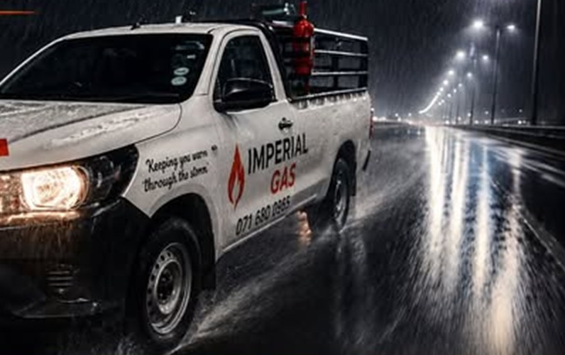 The Imperial Gas delivery bakkie on a wet Mitchells Plain road at night, headlights on, brand and phone number on the door